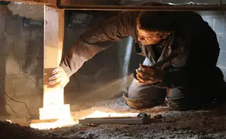 A professional inspecting wooden beams under the floor of a structure in Detroit, MI