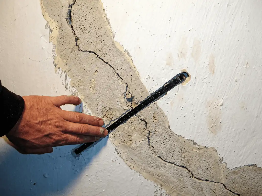 A wall with a large crack is being inspected by a professional in Detroit, MI