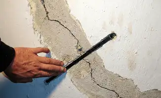 A wall with a large crack is being inspected by a professional in Detroit, MI